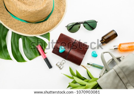 Flatlay with notebook, dark glasses, grey backpack, cosmetics, straw hat and monstera leaves, holiday or vacation concept. White background