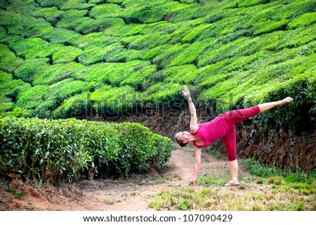 Yoga ardha chandrasana half moon pose by woman in red cloth on tea plantations in Munnar hills, Kerala, India