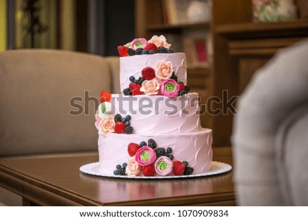 Beautiful elegant three tiered pink wedding cake decorated with berries and flowers. The concept patisserie floristic from sugar mastic