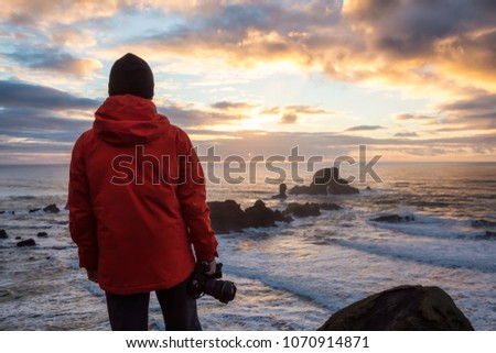 Photographer with a camera is taking pictures during a vibrant and colorful winter sunset. Taken in Ecola State Park near Canon Beach, Oregon Coast, United States of America.