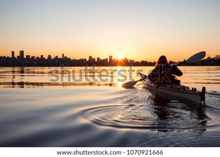 Adventurous girl on a sea kayak is kayaking during a vibrant sunny sunrise. Taken in Downtown Vancouver, British Columbia, Canada.