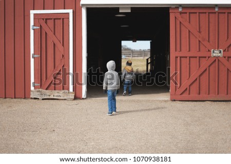 Young boys entering a red cow barn with no smoking sign on a farm during a cloudy winter day.