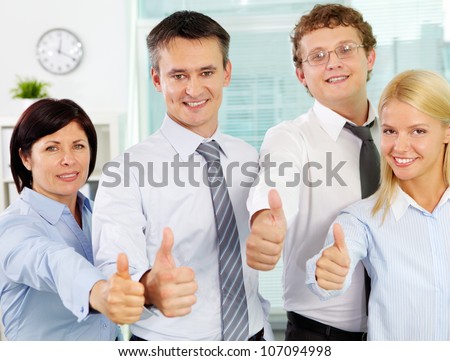 Group of successful businesspeople showing thimbs up and looking at camera with smiles