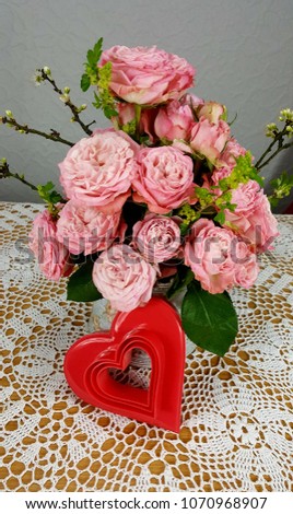 Bouquet of pink roses in a metal jug on a crochet tablecloth and a red heart.