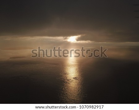 Sun shining through the clouds and fog during sunrise on to the ocean near islands