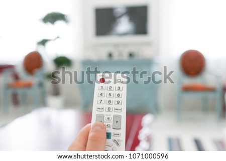 Using white remote control. Program switching or button pressing on TV keypad. Bright living room. Morning european home.