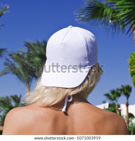 Young girl in a white baseball cap on a background of blue sky and palm trees. White baseball cap mockup. Close-up Royalty-Free Stock Photo #1071003959
