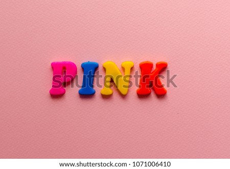 
word 'pink' from plastic colored magnet letters on pink paper background