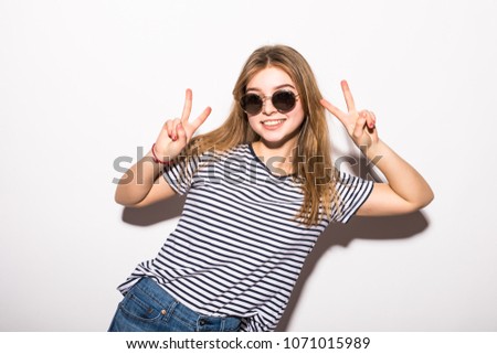 Funny casual teenager girl wearing fashion sunglasses gesturing victory isolated on a white background