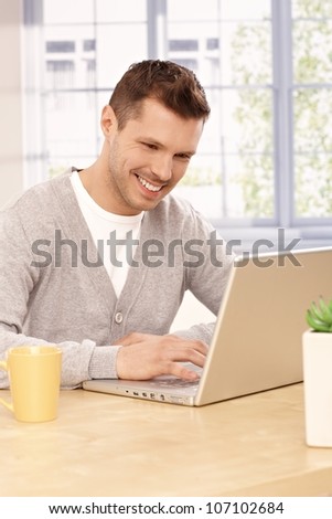 Young man using laptop computer at home, smiling.