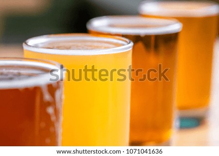 Side view close up on a freshly poured unfiltered pilsners, in a diagonal row of rainbow color pale ales, in a tasting flight of craft beer, at a local brewery