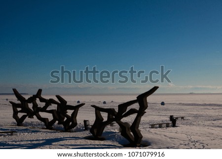 Winter view of empty beach covered with snow and concrete abstract sculpture. Blue sky and deserted frozen bay background. 