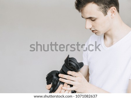 A young man holds a photo camera and looks at it. ?solated on gray background