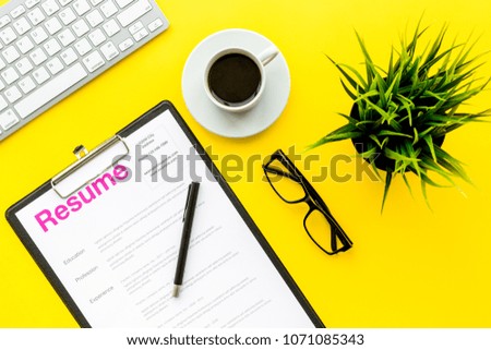 Review resumes of applicants. Resume on yellow work desk with coffee, glasses, keyboard top view