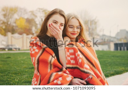 two beautiful and stylish girls sitting in the autumn park near water