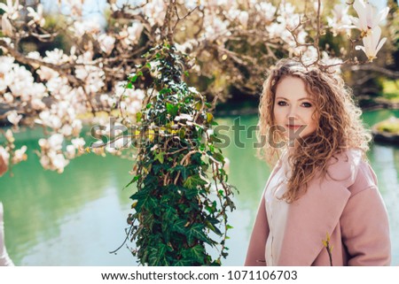 beautiful curly young woman walking in the park, enjoying blossoming trees and a pond, smiling