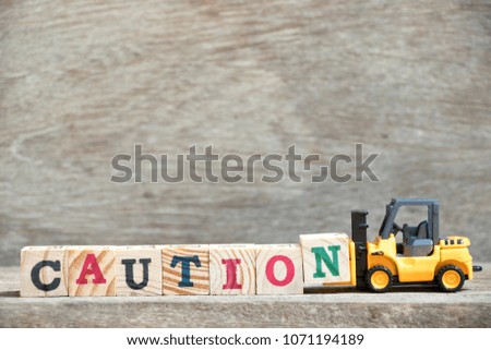 Toy forklift hold letter block N to complete word caution on wood background