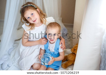A sweet girl and her brother at home. Light children's room with a white interior, flowers and toys