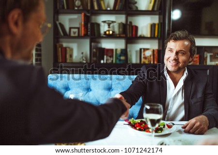 Successful businessmen shaking hands during business lunch at restaurant.