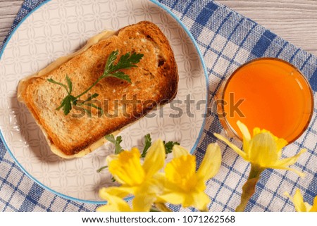 Good and delicious food and beverages for breakfast. Toast with butter and cheese on plate, yellow daffodils and glass of orange juice on kitchen napkin. Top view