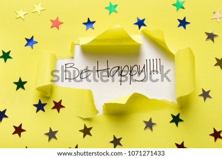 Inspirational phrase Be happy appearing behind torn yellow paper with small glittering stars. Quote for greeting card, banner, poster or clothing design, copy space