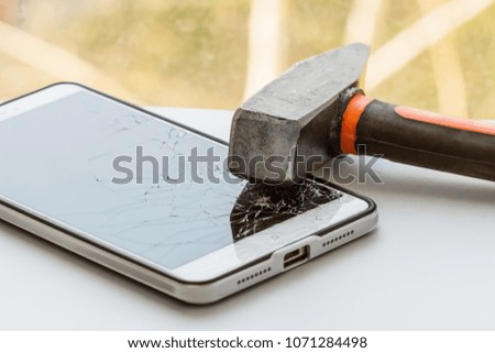 A hammer is on the smartphone with a broken screen. The concept of electronics repair. Closeup, selective focus