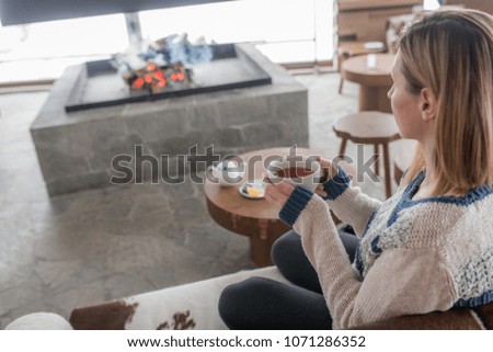 Woman drinking tea and looking at fgireplace at winter;