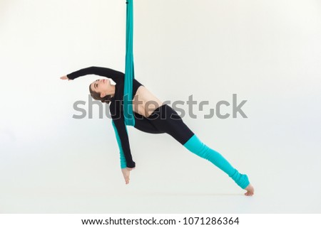 Sporty woman practicing fly yoga warrior asana over white background in fitness studio, copy space. Health, sport, yoga concept