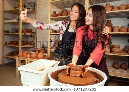 two beautiful potter women doing selfie on the phone. girlfriend works with clay on a potter's wheel and take pictures of herself in a pottery workshop. fun, creativity and clay