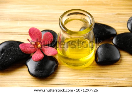 Spa setting with bottle oil, red orchid, black stones on wooden background
