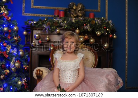 girl in white with pink dress sitting in chair near Christmas tree in Christmas