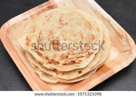 Popular breakfast dish Kerala Parotta or Porotta is a layered flatbread made from maida flour, served in organic plate or platter in South India. Delicious with side dish chilli chicken or chilli beef Royalty-Free Stock Photo #1071321098