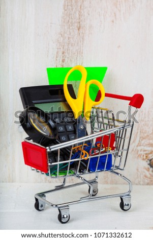 Items for school in a shopping cart on a wooden background. 
