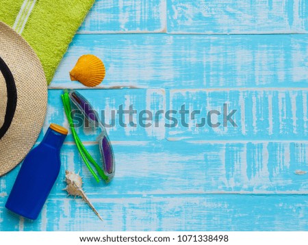 Beach accessories including sunglasses, sunscreen, hat beach, shell and green towel on bright blue wooden background for summer holiday and vacation concept.