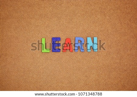 Colorful words concept. The word “learn” on brown plywood background.