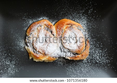 Bun on a black plate with powdered sugar on black background