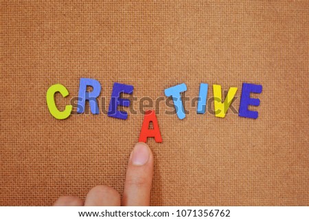Colorful words concept. The word “creative” on brown plywood background. A finger pushing an alphabet to complete the word.