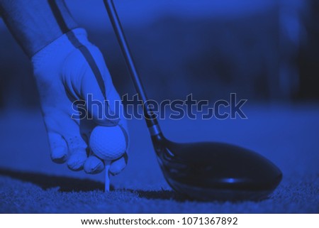 golf player placing ball on tee. beautiful sunrise on golf course landscape  in background duo tone