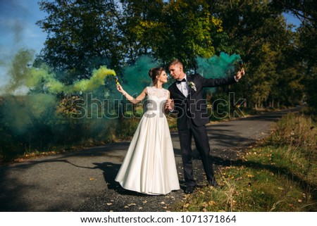 Wedding couple hold colored smoke in their hands in the middle of alley