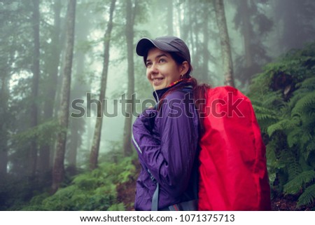 Photo of smiling girl with backpack in misty forest