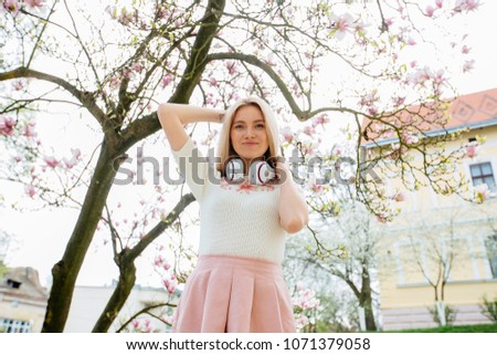 Blond elegant sweden woman with headphones relaxing free time under blossom magnolia tree in beautiful cozy yard or garden. Tenderness concept.