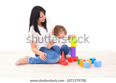 young mother and her infant daughter playing with colored toy bricks on floor indoors at white wall
