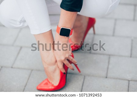 Photo of female hands touching screen generic design smart watch. Film effects, blurred background, red strap