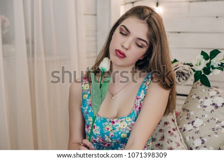 Young brunette with a tulip in her hand. Romantic interior.