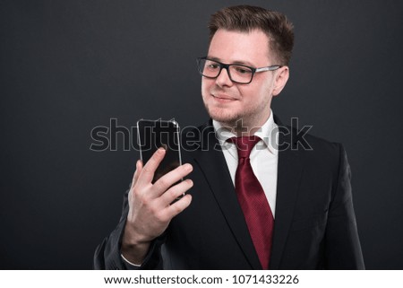 Business young man looking at black smartphone and smiling on black background with copy advertising area