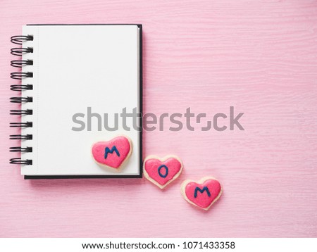 Heart-shaped cookie with the word MOM, covered with bright glaze, sketchbook with a blank page for Your inscription. Top view. Pink, isolated background. The concept of a happy family