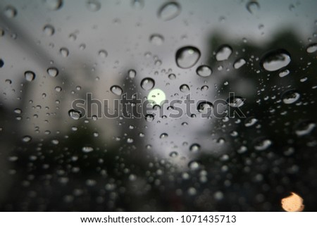 Defocused image, water drops on the windshield, traffic in the city on a rainy day, car windshield view, colorful bokeh, dark background.