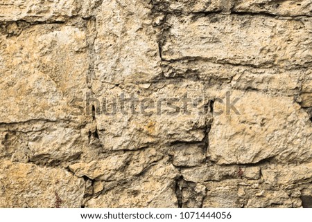 A fortress wall made of stones of the same size and shape. Stones of yellow color from limestone. The stones are joined together with cement.