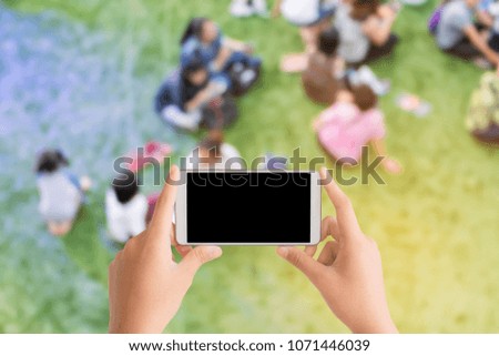 woman use mobile phone and blurred image of people sit on the grass field with blue and orange lights from the spotlights in the event look from top view