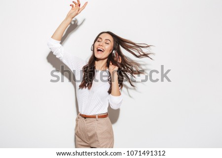 Portrait of a happy asian businesswoman listening to music with headphones and dancing isolated over white background
